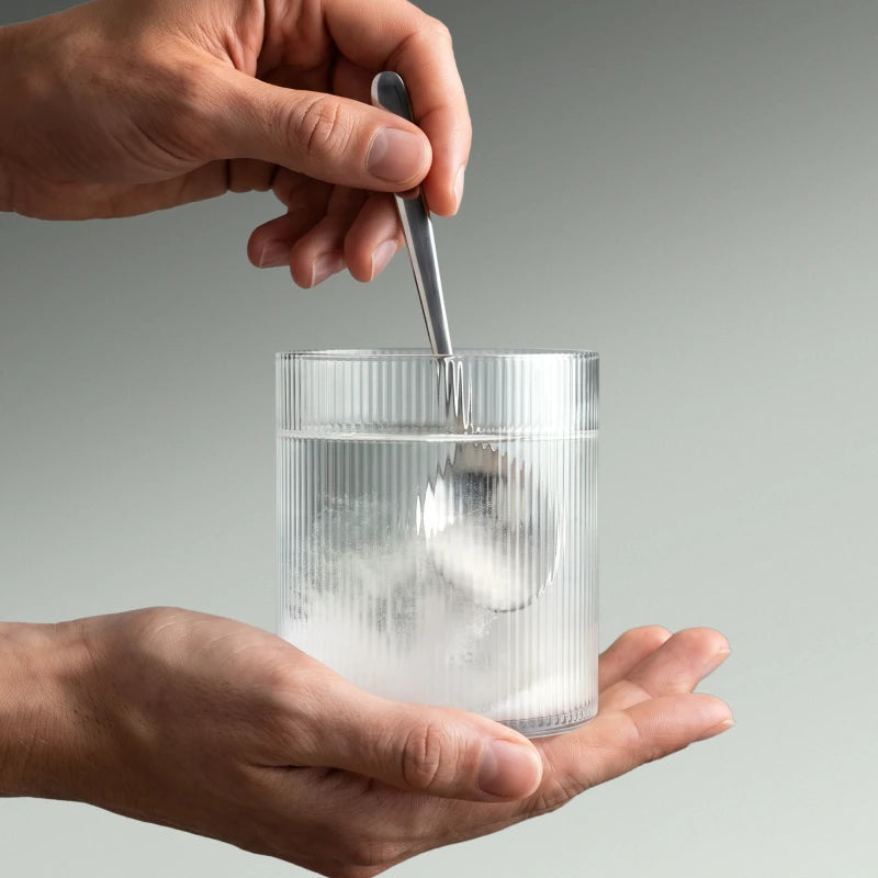 Photo de mains en train de diluer de la créatine dans un verre d'eau.