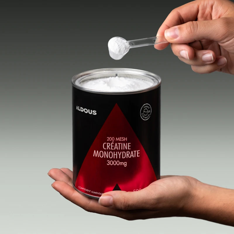 Photo de mains prenant une cuillère doseuse de créatine dans le pot de Creatina Aldous